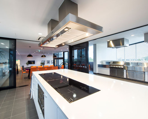 A sleek, modern outdoor kitchen with stainless steel benches, cabinets and rangehoods